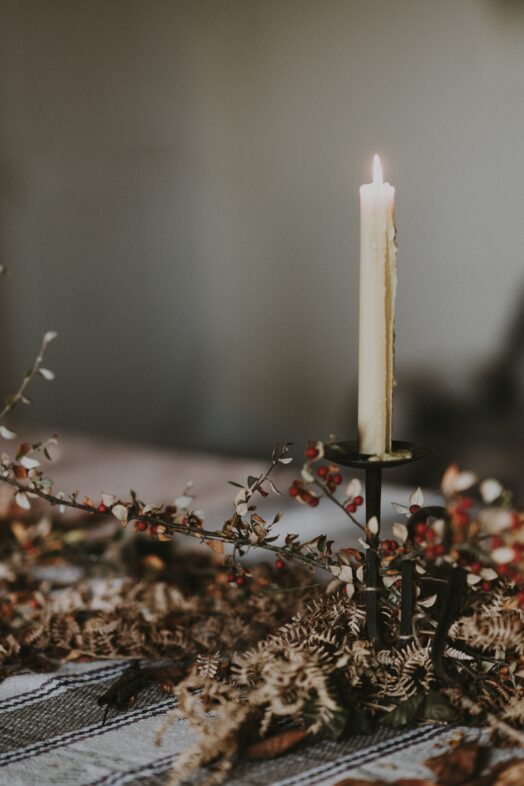 Ett tänt stearinljus i en ljusstake omgiven av torkade blommor.
