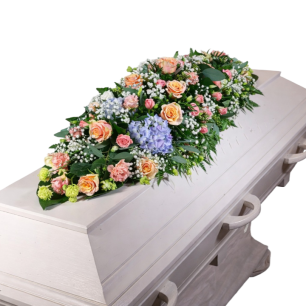 En vit kista dekorerad med ett stort blomsterarrangemang i pastellfärger, inklusive rosa och blå blommor samt grönt lövverk.